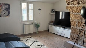 Un saló amb una paret de pedra, un sofà negre, una televisió i una creu a la paret.