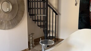 Un bany modern amb una banyera autònoma, una escala espirals negra i un mirall decoratiu a la paret.