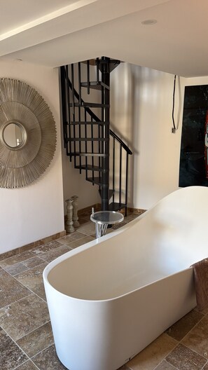 A modern bathroom with a freestanding bathtub, a black spiral staircase, and a decorative wall mirror. - Dream Home for Rent in Southern France (Soubès)