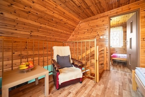 Ein Holzhütten-Interieur mit einem Holzstuhl, einem Tisch mit Obst, einem Bett und einer Treppe.