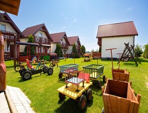 A playground with various play equipment, including swings and a slide, in a grassy area with houses in the background. - Two-story Holiday Homes With Terraces, Playground (Mielno)