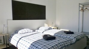 Ein Schlafzimmer mit einem Bett, zwei Nachttischen, einer Pendelleuchte, einem Kleiderschrank und einer großen, dunklen Wand.