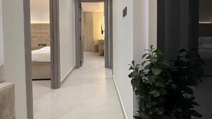 Un pasillo con una planta en maceta, una cama a la vista al fondo y una puerta a la derecha.
