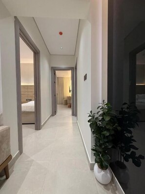 Corredor com planta em vaso, cama visível ao fundo e porta à direita.