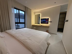 A modern hotel room with a large bed, a built-in TV, a mirror, and a view of the outdoors. - OrbitNet - Asasiat 36 (Madina)