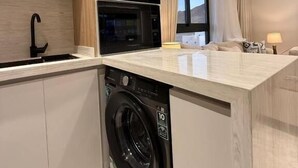 A modern kitchen with a built-in washer, wooden cabinets, and a large window. - OrbitNet - Asasiat 36 (Madina)