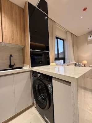 A modern kitchen with a built-in washer, wooden cabinets, and a large window. - OrbitNet - Asasiat 36 (Madina)