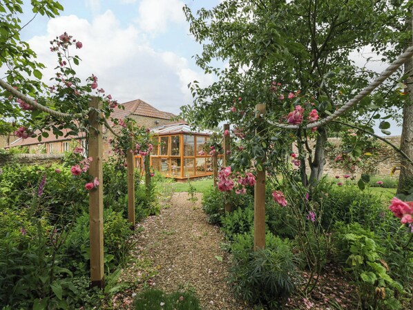Ein Garten mit einer Holz-Pergola, einem Wintergarten und einem Kiesweg.