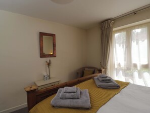 Habitación de hotel con cama, mesita de noche, espejo, ventana con cortinas y una planta pequeña.