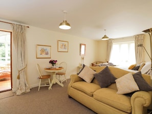 A living room with a sofa, a dining table with chairs, a ceiling light, and a window with curtains.