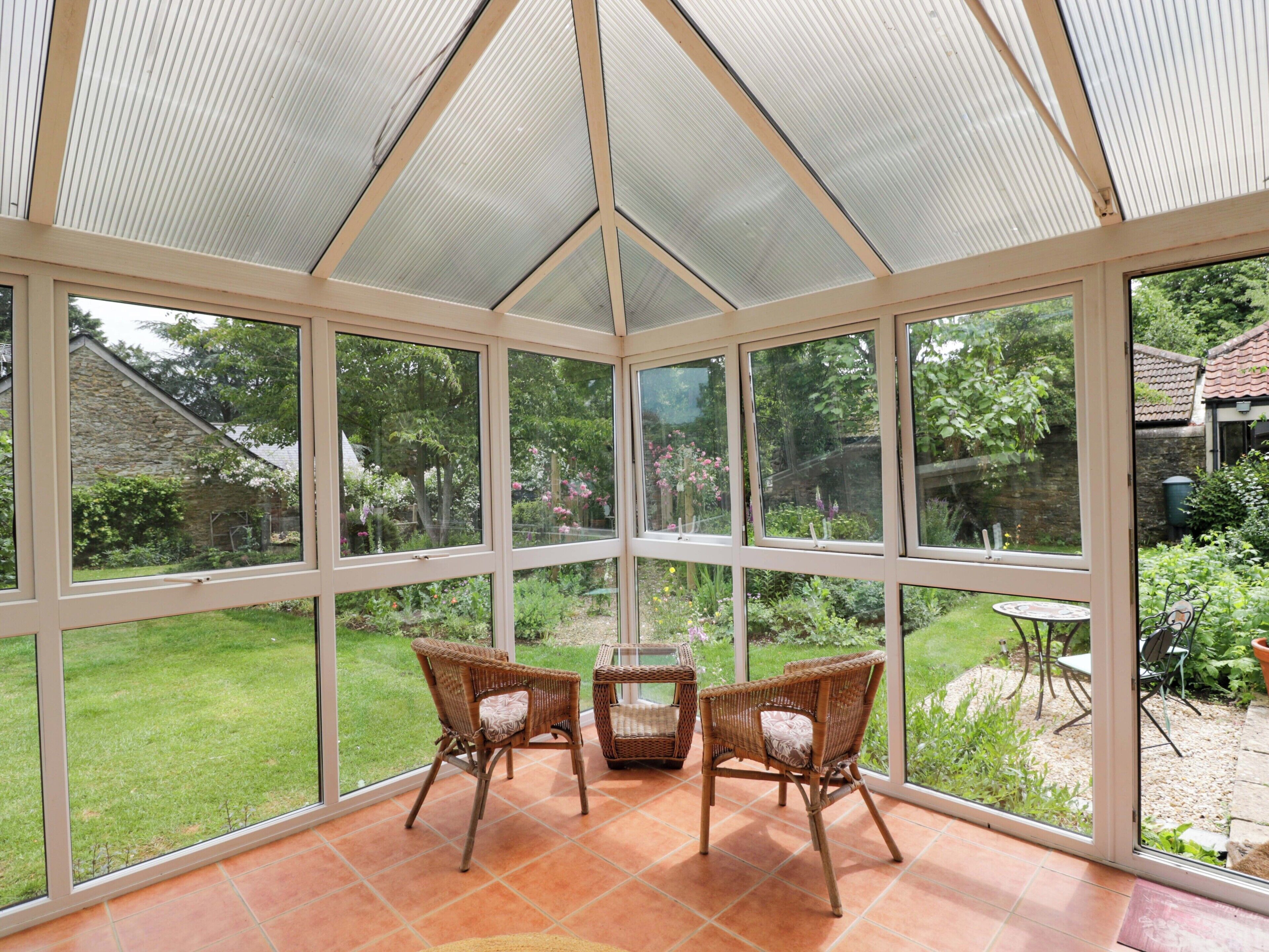 A conservatory with a glass ceiling, wicker chairs, and a view of a garden.
