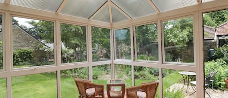 A conservatory with a glass ceiling, wicker chairs, and a view of a garden.