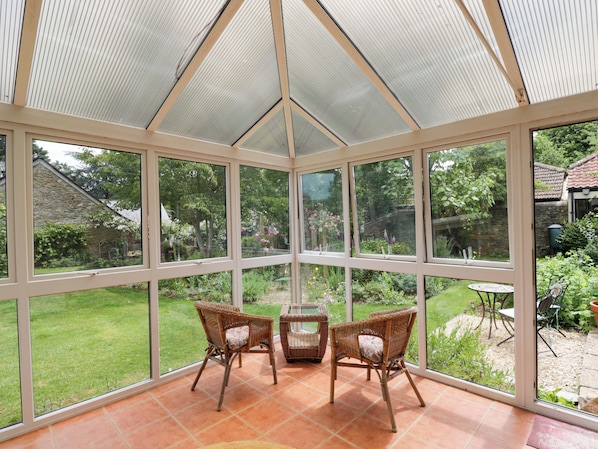 A conservatory with a glass ceiling, wicker chairs, and a view of a garden.