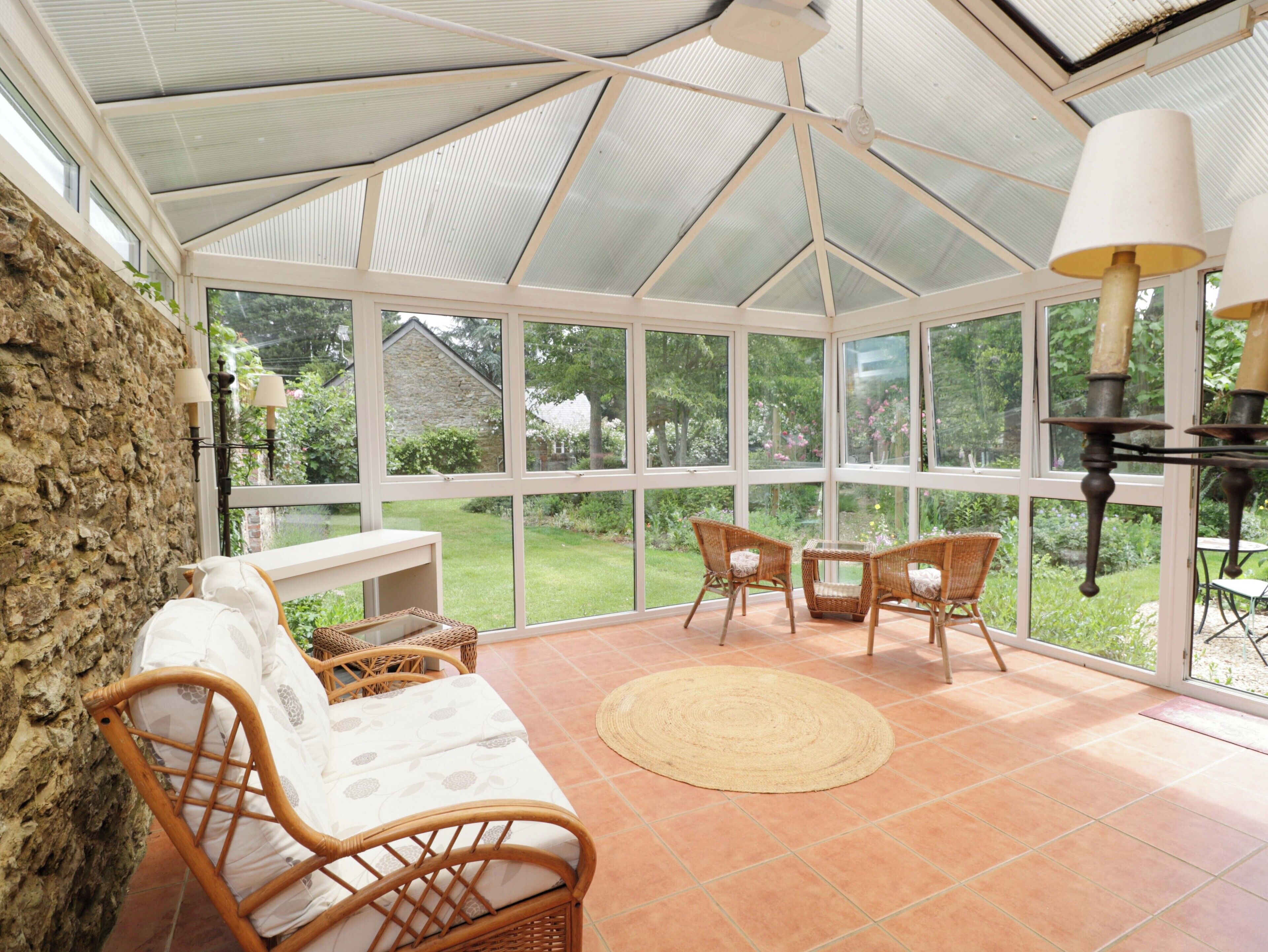 A conservatory with a stone wall, wicker furniture, and a view of the garden.