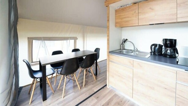 Une cuisine compacte comprenant un coin repas, des meubles de rangement en bois, un évier et une machine à café.