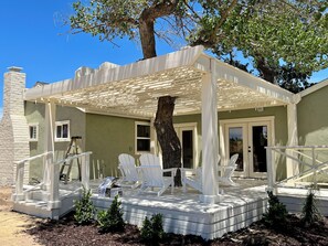 Ein Haus mit überdachter Veranda, weißen Gartenstühlen, einer Leiter und einem Baum.