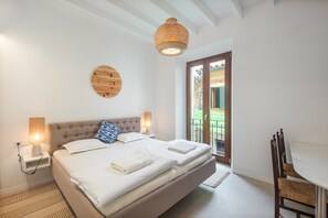 A bedroom with a bed, bedside lamps, a round wall decoration, a window with a view, and a small table with a chair. - Holiday Home 'Rectoria 8' with Mountain View, Wi-Fi and Air Conditioning (Valldemossa)