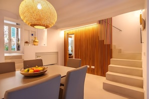 A modern dining area with a wooden table, chairs, a fruit bowl, and a woven light fixture.