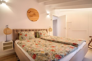 Un dormitorio con cama, dos lámparas de noche, un espejo redondo en la pared y una puerta.