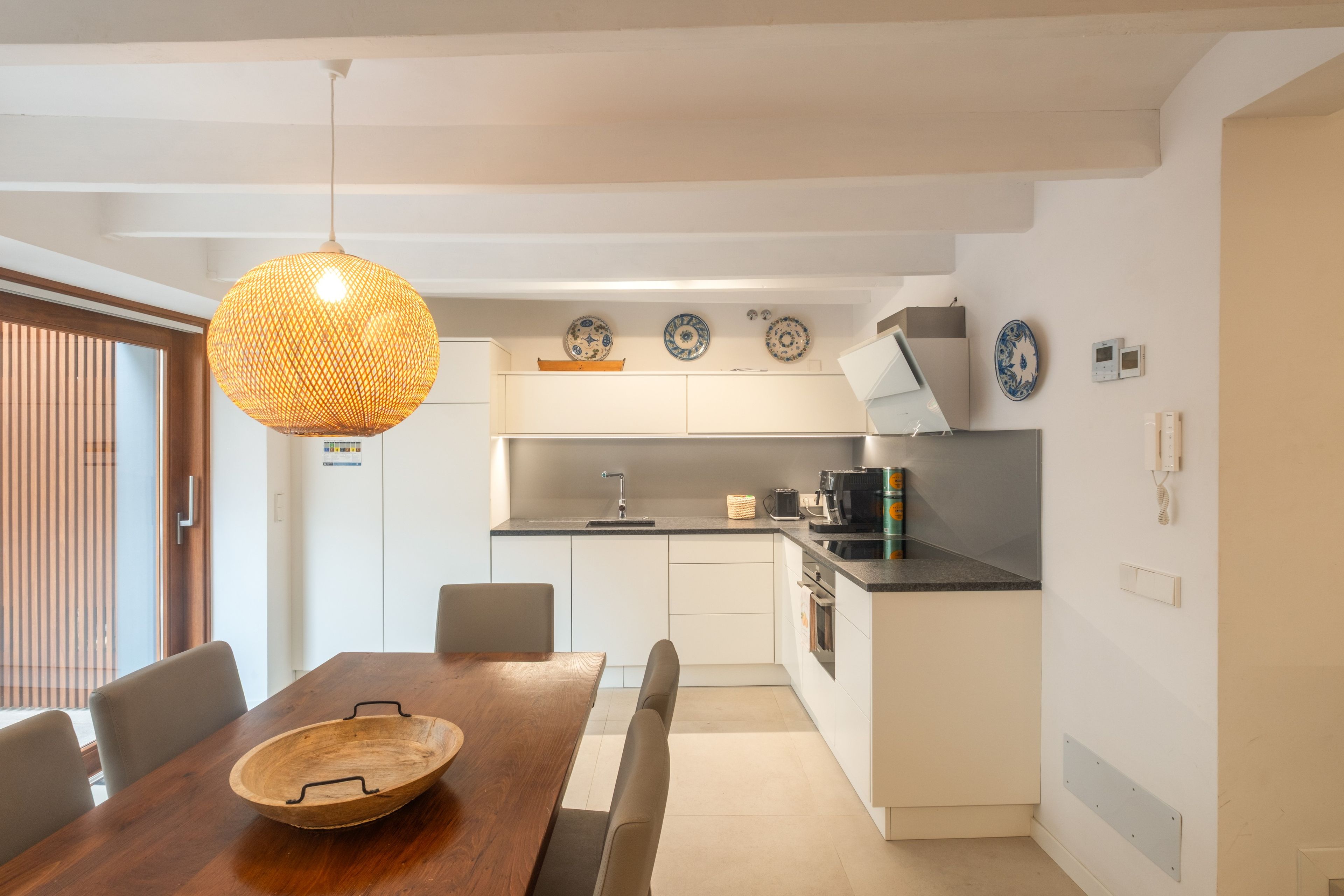 Ett modernt kök med vita skåp, ett matbord i trä och en hängande lampa.