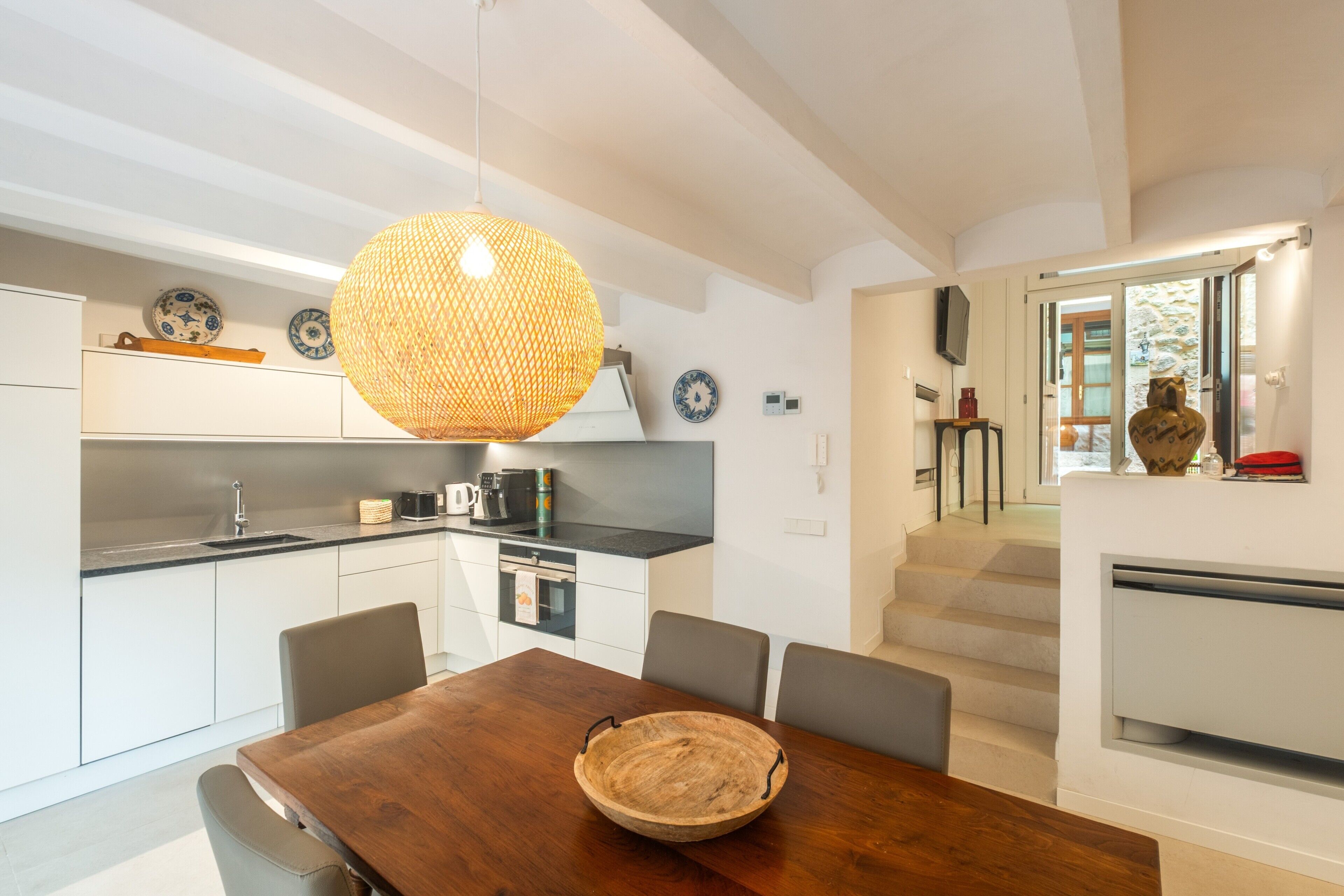A modern kitchen with white cabinetry, a wooden dining table, and a hanging light fixture.
