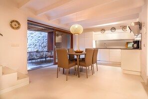 Een moderne keuken met witte kasten, een eethoek met een ronde tafel en stoelen, en uitzicht op een balkon.