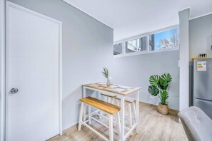 Eine kleine Küche mit einem weißen Tisch und einer Bank, einem Blumentopf und einem Kühlschrank.