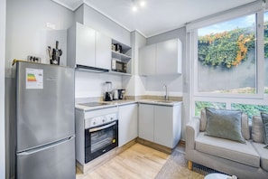 Eine moderne Küche mit Kühlschrank, Backofen und Kaffeemaschine, sowie eine Sitzecke mit Blick auf Grünflächen.