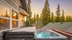 Ein Whirlpool mit Schlauch, eine Holzterrasse und Blick auf hohe Bäume.