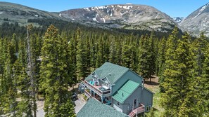 A lodge with a green roof, a deck, and a mountain backdrop. - Summit County Escape | Private Hot Tub+ Deck (Breckenridge)