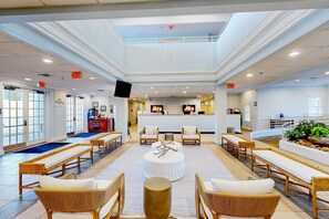 A spacious lobby with wicker furniture, a central round table, and a reception desk.