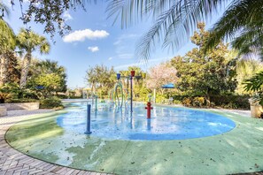 A water play area with a circular blue surface, surrounded by palm trees and other greenery.