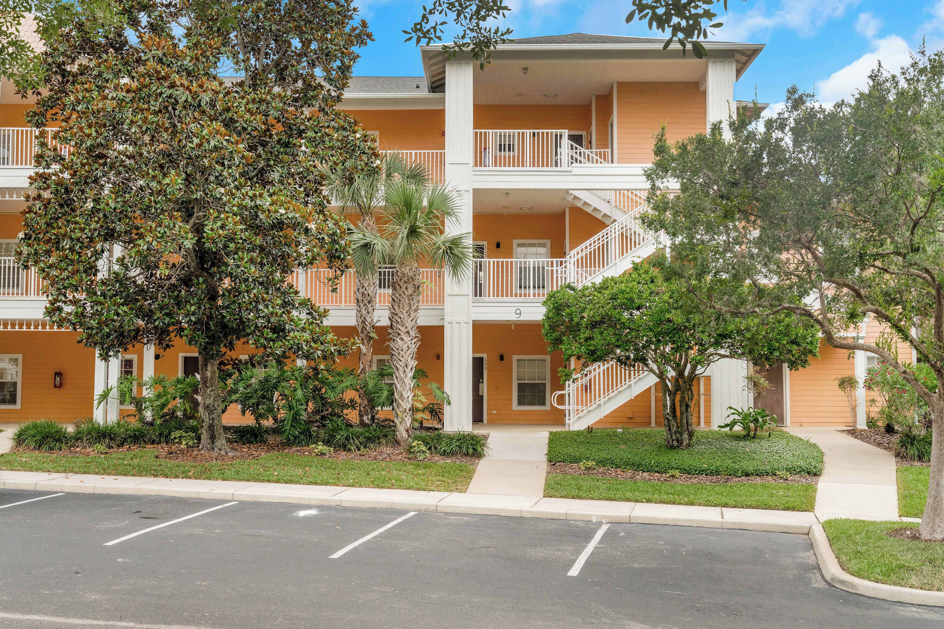 A multi-story hotel with balconies, a parking lot, and landscaped greenery.