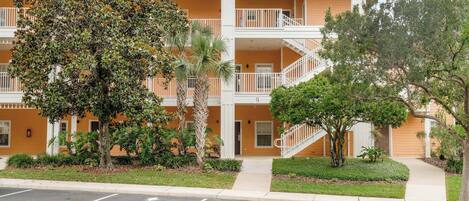 A multi-story hotel with balconies, a parking lot, and landscaped greenery.