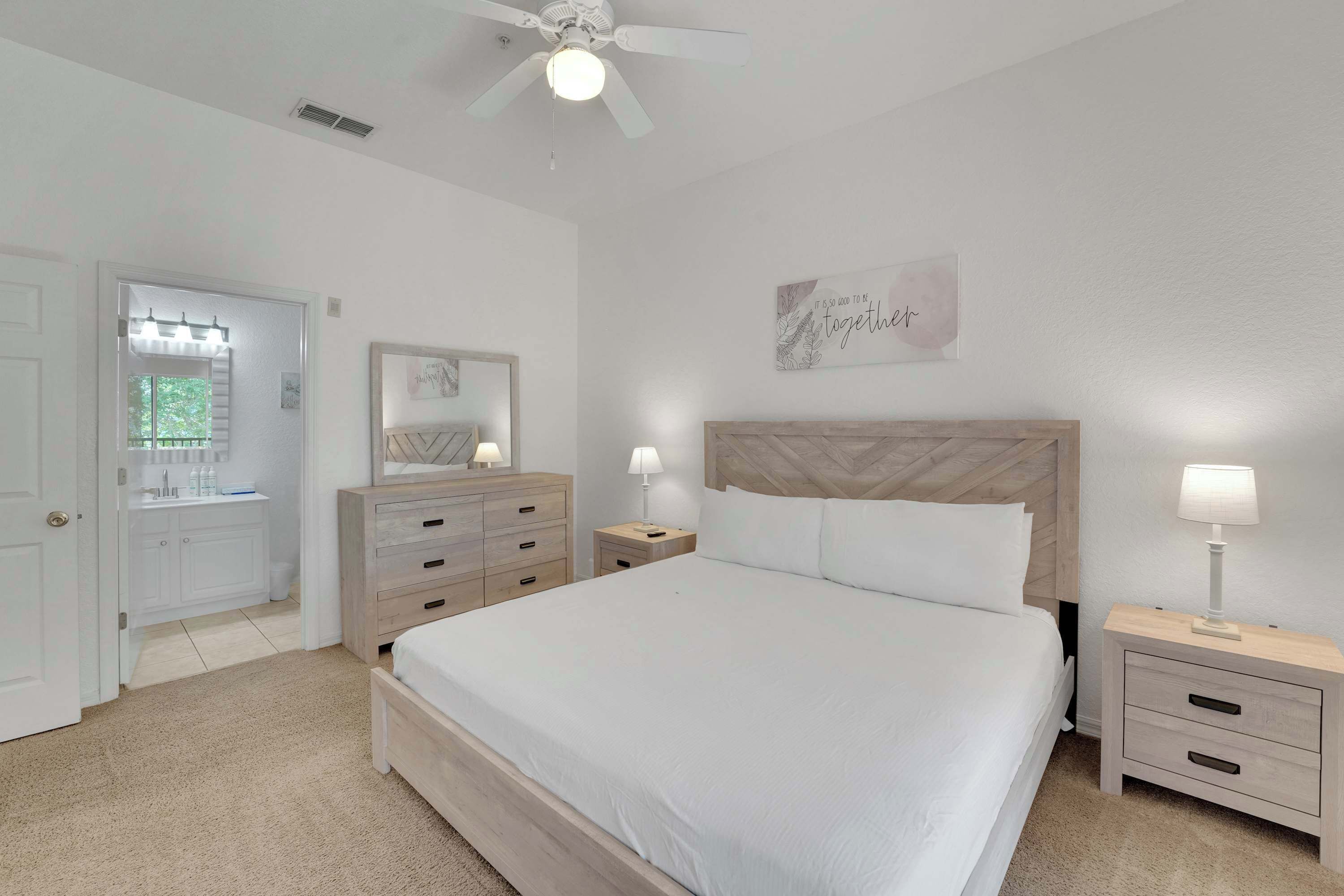 A bedroom with a bed, nightstands, a dresser, a ceiling fan, and a wall with a motivational quote.