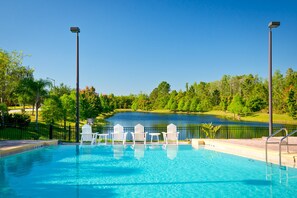 A swimming pool with white chairs and a view of a lake and trees. - 2nd Floor Condo w/ Balcony, Shared Pools, hot Tub, Sauna, Gym, Near Theme Parks (Kissimmee)