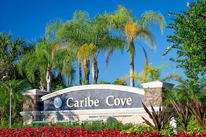 A sign for "Caribe Cove" with a stone arch and palm trees in the background. - 2nd Floor Condo w/ Balcony, Shared Pools, hot Tub, Sauna, Gym, Near Theme Parks (Kissimmee)
