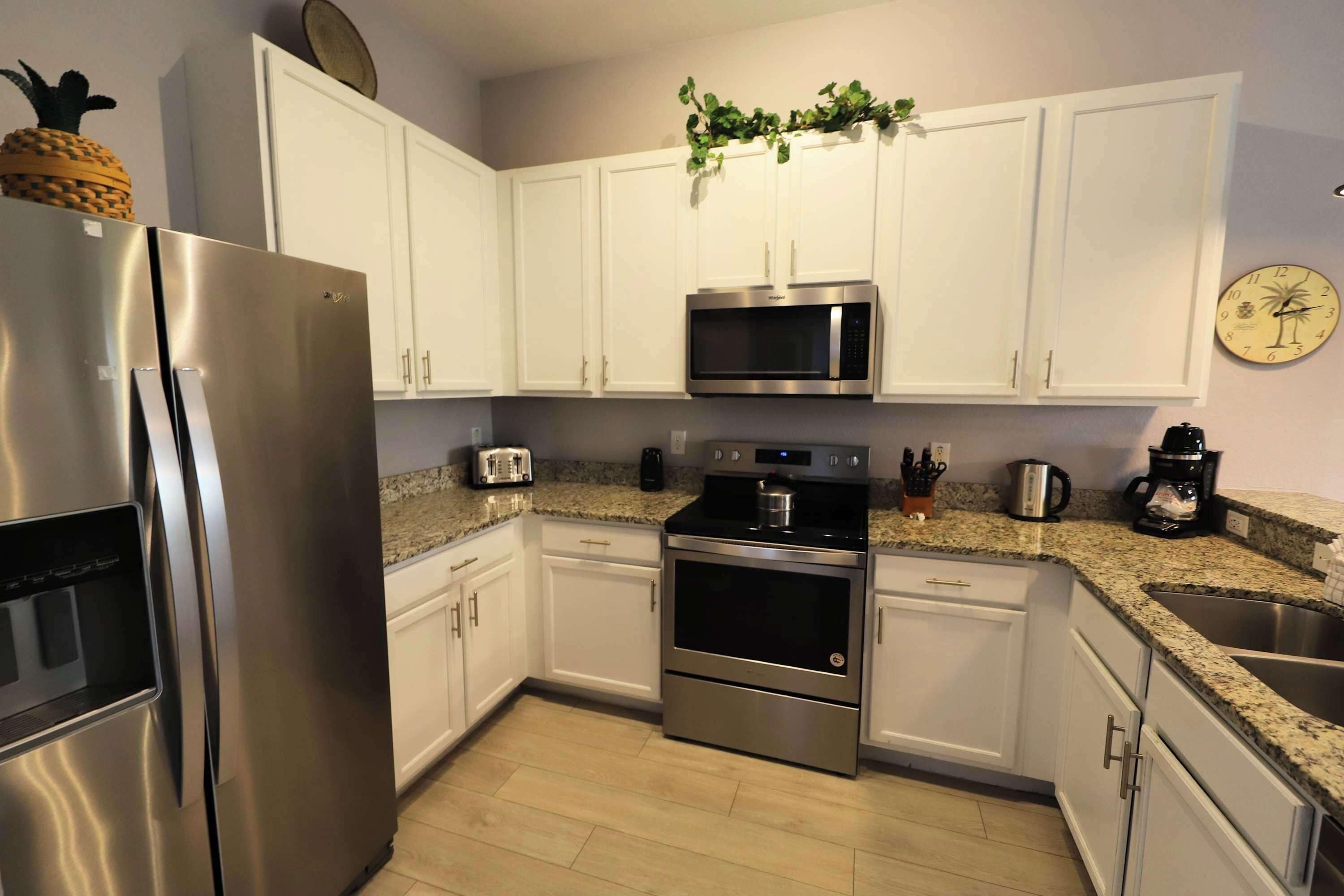 Una cocina con armarios blancos, electrodomésticos de acero inoxidable, encimera de granito y un reloj en la pared.