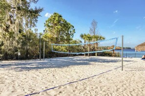 Un terrain de beach-volley avec un filet, entouré d’arbres et sous un ciel dégagé.