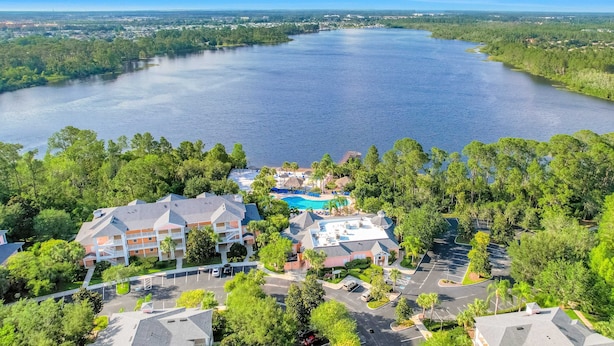 A hotel with a swimming pool, surrounded by lush greenery and a large lake. - Beautiful Condo With Pool, hot Tub, Central AC & W/D - Short Drive to Disney (Davenport)