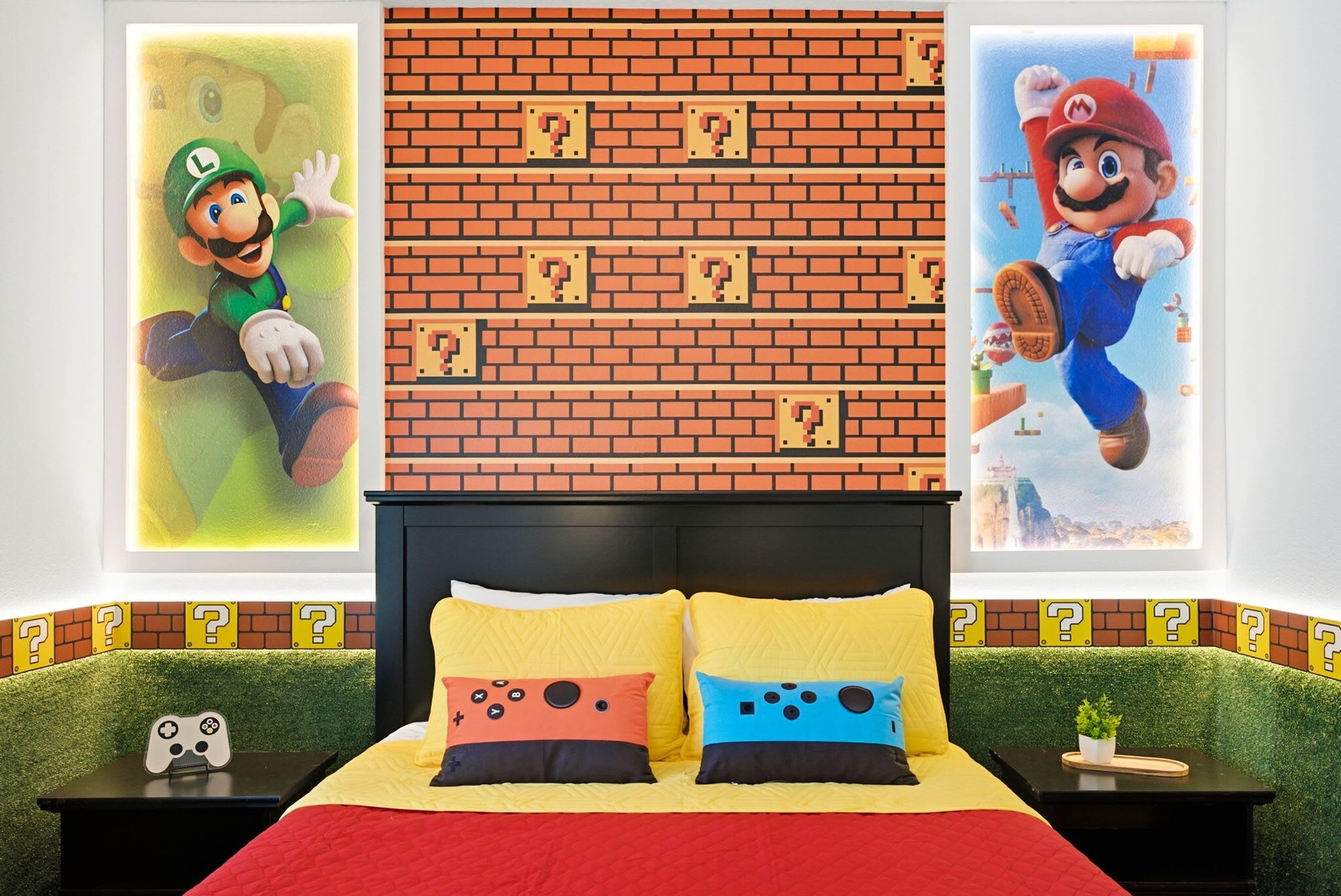 Un lit avec une literie jaune et rouge, une tête de lit à motifs de briques et deux oreillers décorés avec des motifs de manettes de jeu.