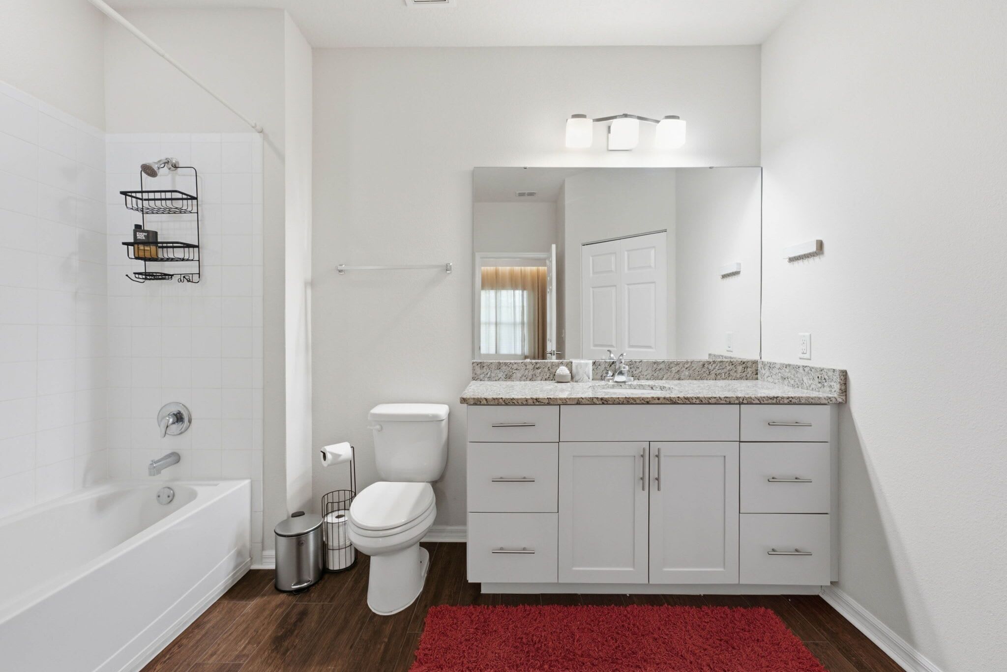 A modern bathroom with a bathtub, toilet, vanity with drawers, and a red rug.
