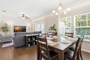 Ein Essbereich mit einem Holztisch, gedeckt für vier Personen, einem grauen Sofa und einem Deckenventilator.