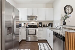 A modern kitchen with stainless steel appliances, white cabinets, a granite countertop, and a clock on the wall. - Beautiful Home, Themed Rooms, Prime Location (Kissimmee)