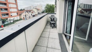 En balkong med ett bord och stolar, utsikt över gatan och en byggnad med flera våningar.