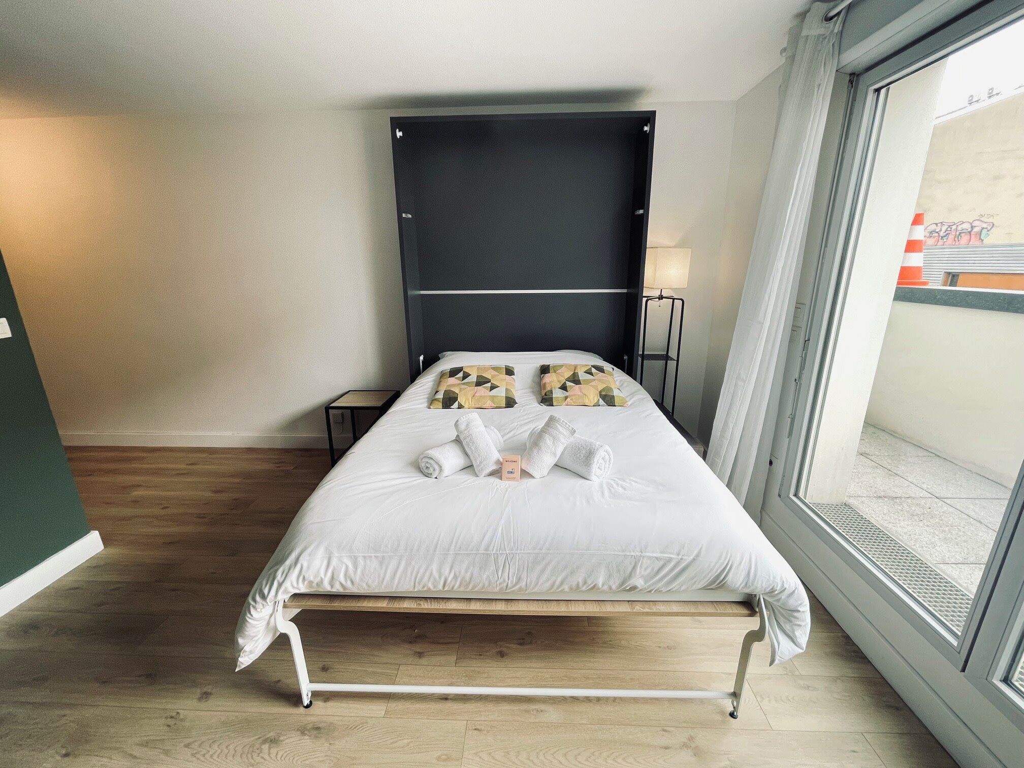 A neatly made bed with pillows, a bedside lamp, and a view through a window.