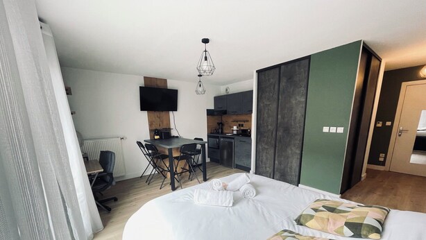 Ett hotellrum med en säng, ett skrivbord, en stol, en TV och ett litet kök.