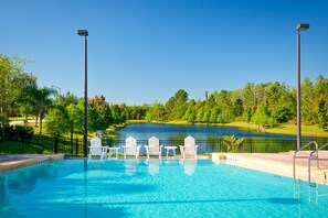 Piscina com cadeiras brancas e vista para um lago.