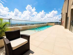 Ein Pool auf dem Dach mit Glasgeländer, einem Korbstuhl und einem Blumentopf.