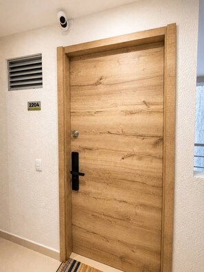 A wooden door with a number plate, a wall-mounted light switch, and a vent above it. - Mediterranean Suite | Sea View & Pool (Cartagena)